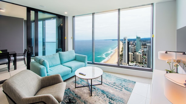 A modern living room with a large window overlooking a beach and cityscape.