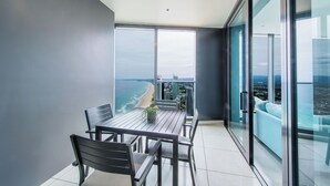 A balcony with a table and chairs, a potted plant, and a view of the ocean and cityscape.