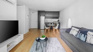 A modern living room with a flat-screen TV, a grey sofa, and a dining area with a table and chairs.