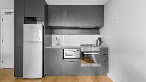 A modern kitchen with grey cabinetry, a built-in oven, and a stainless steel refrigerator.