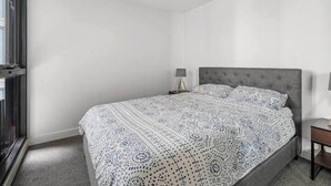A bedroom with a large bed, a nightstand, a lamp, and a window.
