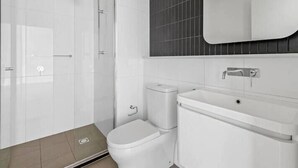 A modern bathroom with a glass shower enclosure, a white toilet, and a sink with a mirror above.