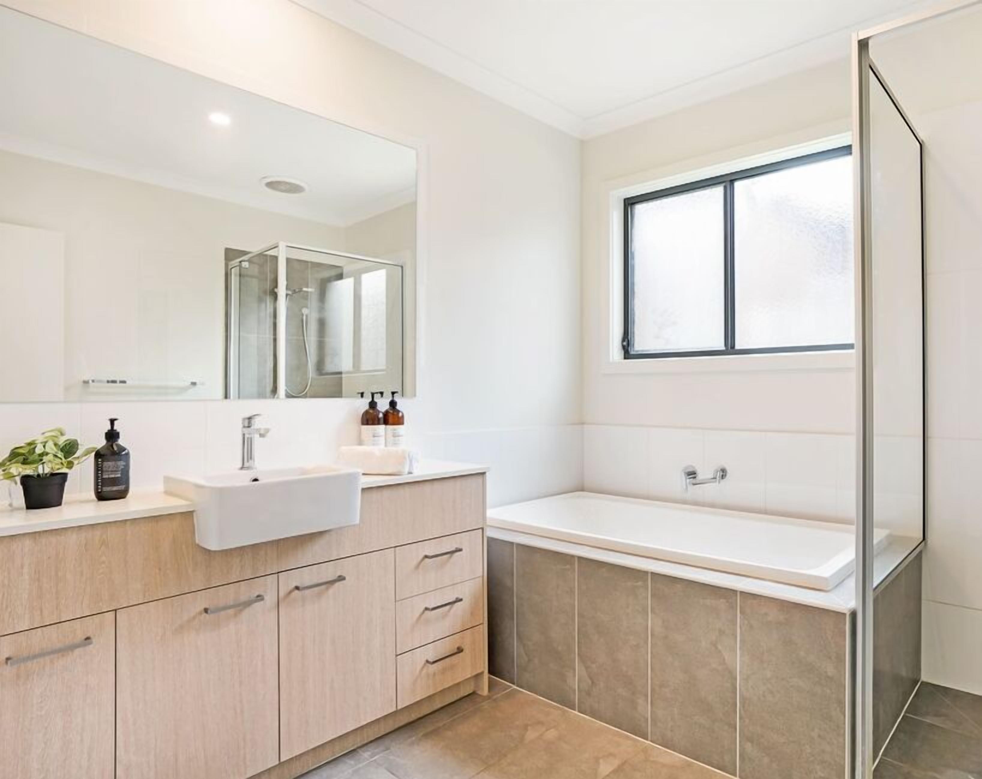 Un baño moderno con un espejo grande, un lavabo, una bañera y una ducha.