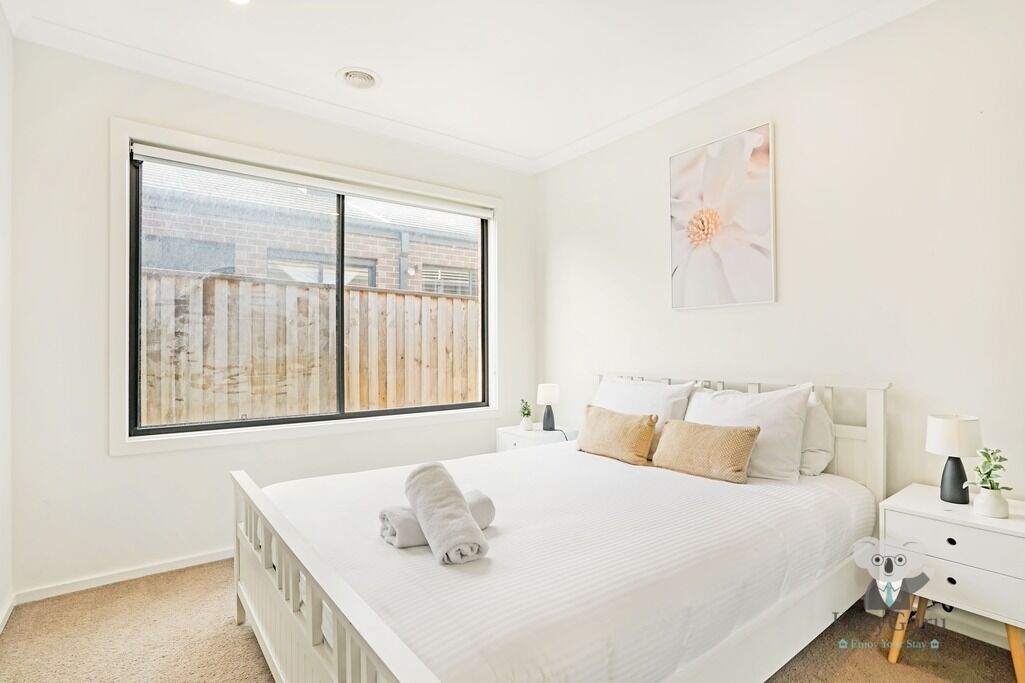Un dormitorio con un ventanal grande, una cama con ropa blanca, una mesita de noche y una lámpara de pared.