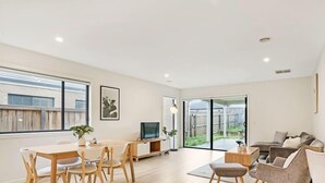 A spacious living room with a dining area, a sofa set, and a TV. - Kozyguru | Greenvale | Charming 7 Bed House (Greenvale)