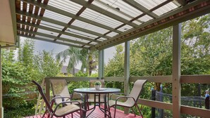 Un patio al aire libre techado con una mesa y sillas, rodeado por una barandilla de madera y vistas a follaje exuberante.