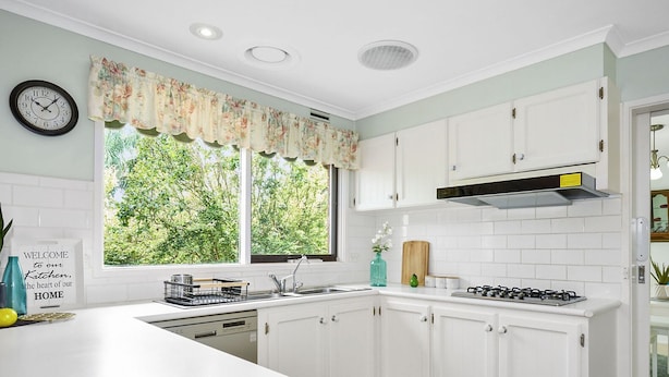 Una cocina con armarios blancos, una estufa, un fregadero y un ventanal con vistas al verdor.