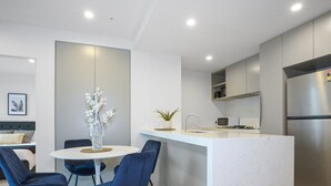 Una cocina moderna con una isla central, un comedor con sillas azules y una cama con cabecera gris.