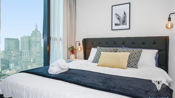 Habitación de hotel con una cama grande, vistas a la ciudad, una obra de arte enmarcada en la pared y una lámpara moderna.