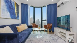 Una sala de estar moderna con un sofá azul, dos sillones, una mesa de centro y un televisor grande.