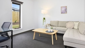 Ein modernes Wohnzimmer mit Glastisch, einer Couch, einem Sessel, einer Lampe und einem Fenster mit Blick auf einen Holzzaun.