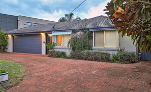 Situated in a suburban area, this single-story house features a garden with shrubs and a small tree.