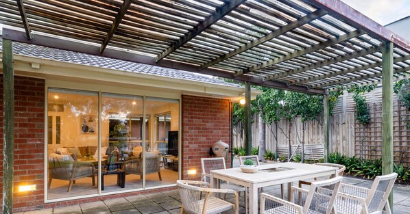 Relax in a covered patio area with a brick wall, wooden pergola, and glass door leading to a cozy interior space.