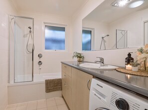 Enjoy a refreshing shower or soak in the standalone bathtub in this bathroom, featuring a sink and digital washing machine.