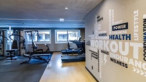 Un gimnasio con equipo de ejercicio, ventanas amplias y gráficos motivacionales en las paredes.