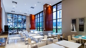 Un espacio interior amplio con varias mesas y sillas, ventanas grandes y un diseño moderno de techo.