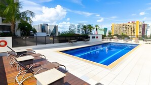 Una piscina en la azotea con sillones reclinables y vistas a la ciudad.