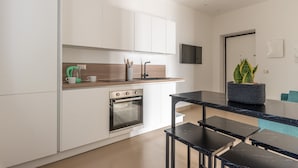 Une cuisine moderne avec des meubles blancs, un four encastré, un plan de travail noir et une table à manger noire avec des bancs.