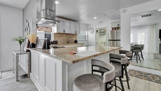 A modern kitchen with white cabinetry, a granite countertop, and a central island with bar stools. - Charming 2-bedroom apartment in lovely DeBary with AC, WiFi (DeBary)