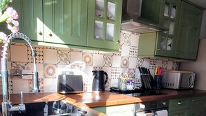 A kitchen with green cabinets, a wooden countertop, a black mat, a sink, a toaster, a kettle, and a microwave.