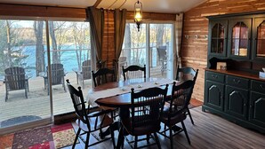 Un espace repas comprenant une table et des chaises en bois, un luminaire suspendu et une vue sur l’extérieur.
