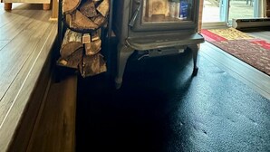 Un poêle à bois avec une pile de bûches à côté, une fenêtre donnant sur l’extérieur et un intérieur en bois.