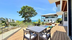 A wooden deck with a table and chairs, a pool, and a view of the ocean.