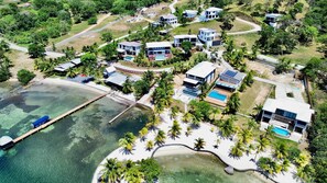 An aerial view of a resort with multiple modern villas, a beach, and clear waters.
