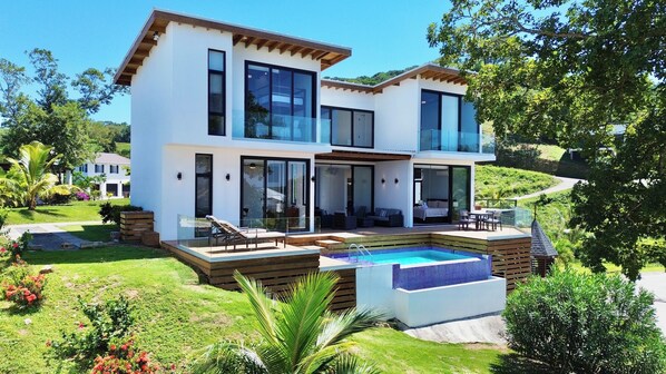 A modern two-story house with a large glass balcony, a swimming pool, and a well-maintained garden.