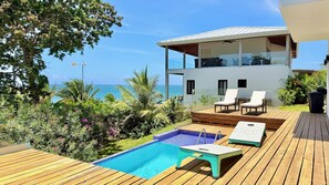 A modern two-story building with a pool, lounge chairs, and a view of the ocean.