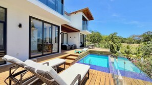A modern house with a pool, outdoor furniture, and a view of the surrounding greenery.
