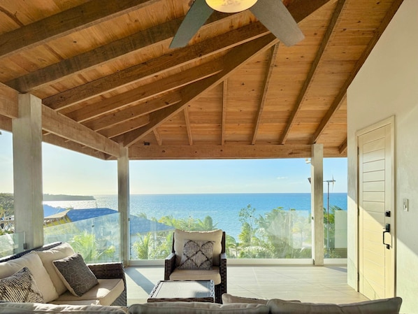 A covered outdoor seating area with a view of the ocean, a ceiling fan, and a door to the right.