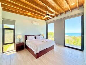 Ein Schlafzimmer mit einem großen Bett, Holzbalkendecke, Deckenventilator und Meerblick.