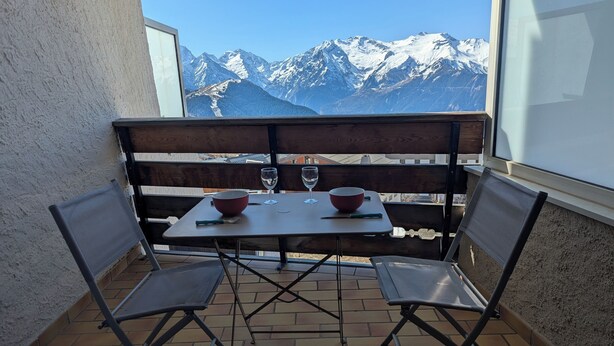 A balcony with a table and chairs, overlooking snow-capped mountains.