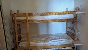 A bunk bed with a wooden frame and white bedding in a room with tiled flooring and white walls.
