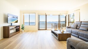 Un salon spacieux doté d’un grand téléviseur, d’un parquet, d’un canapé et d’un balcon offrant une vue sur la mer.