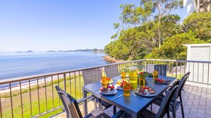 Une table à manger avec vue sur la mer, entourée de chaises et d’une rambarde.