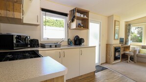 Una cucina compatta con forno a microonde, bollitore e macchina per il caffè. Include un armadietto in legno e un piccolo angolo con una sedia.