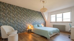 A bedroom with a bed, a chair, a desk, a radiator, and a window.
