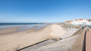 A beach with a promenade, a view of the sea, and a row of buildings with red roofs.