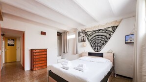 A bedroom with a bed, a wooden dresser, a tapestry, and a door leading to another room. - Jardin Bohème - Jardin, terrasse et cuisine d'été. (Marseille)