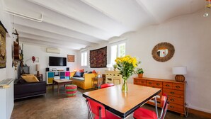 A spacious living area with a wooden dining table, red chairs, a sofa, a television, and a colorful rug. - Jardin Bohème - Jardin, terrasse et cuisine d'été. (Marseille)