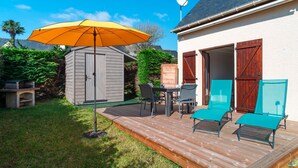 Una terraza de madera con una mesa, sillas, un paraguas amarillo y un cobertizo en un patio trasero.