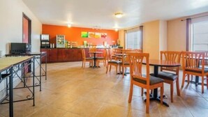 A dining area with wooden tables and chairs, a kitchen in the background, and a tiled floor. - Franklin Inn & Suites (Franklin)