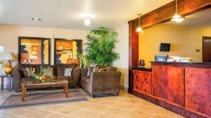 A reception area with a wooden reception desk, a sofa, a coffee table, and a large potted plant. - Franklin Inn & Suites (Franklin)