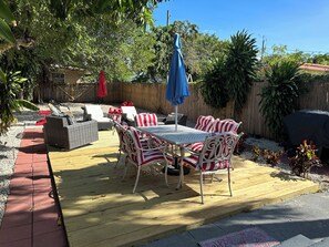 Une terrasse extérieure avec une plateforme en bois, une table blanche avec des coussins à rayures et un parasol bleu.