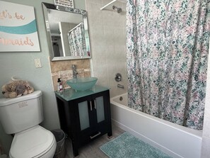 Une salle de bain avec un lavabo en verre, des toilettes, une baignoire et un rideau de douche.