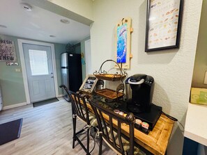 Una kitchenette con cafetera, refrigerador y un panel de menú en la pared.