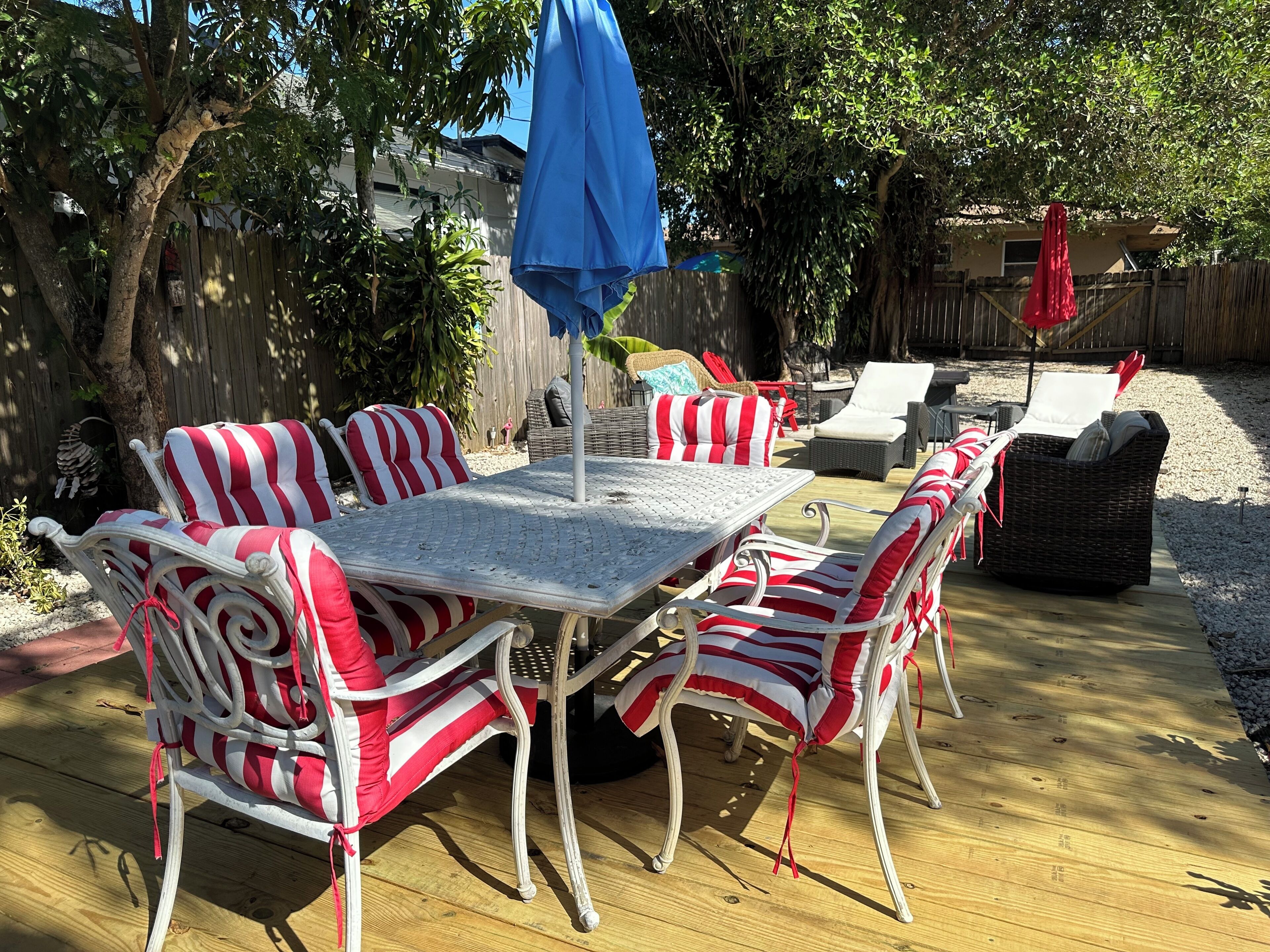 Un patio con mesa y sillas, una sombrilla azul y un cojín a rayas rojas y blancas.