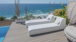 Terraza de madera con dos sillones blancos y una piscina.